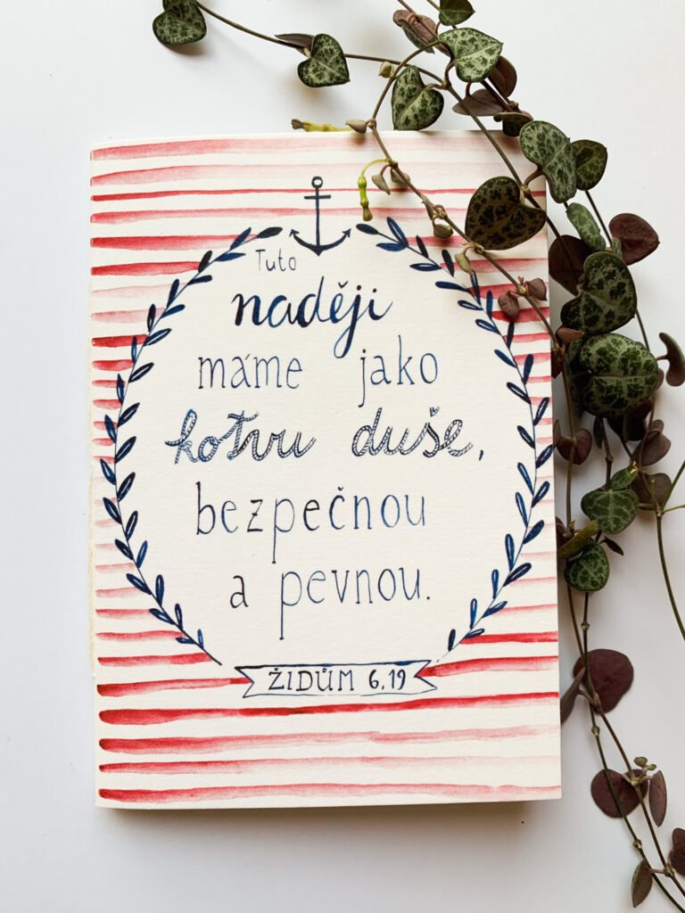 Ilustrovaný křesťanský sešit s biblickým veršem v námořnickém stylu. Ručně psaný biblický verš "Tuto naději máme jako kotvu duše, bezpečnou a pevnou." Židům 6, 19. Kolem verše je námořnicky modrý rámeček s lístečky a kotvou, na pozadí červeno bílé pruhy.